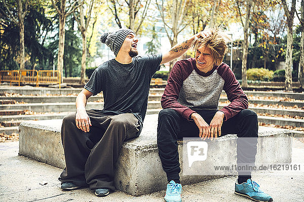Lächelnde  männlich aussehende Haare eines Freundes  der in einem öffentlichen Park sitzt