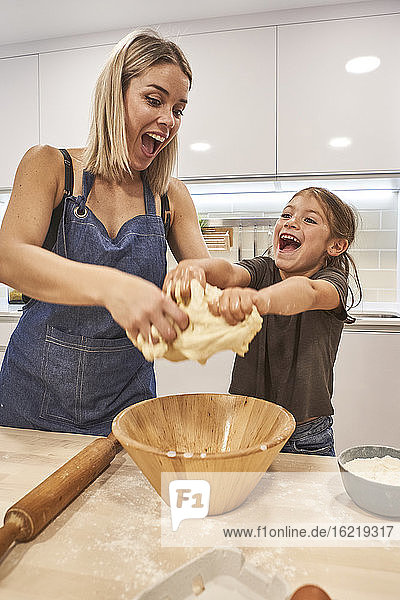 Verspielte Mutter und Tochter schreien beim Kneten von Pizzateig in der Küche zu Hause