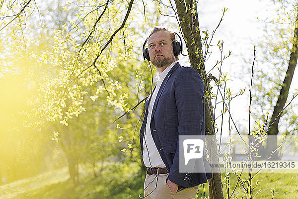 Männlicher Unternehmer hört Musik  während er an einem sonnigen Tag in den Park blickt