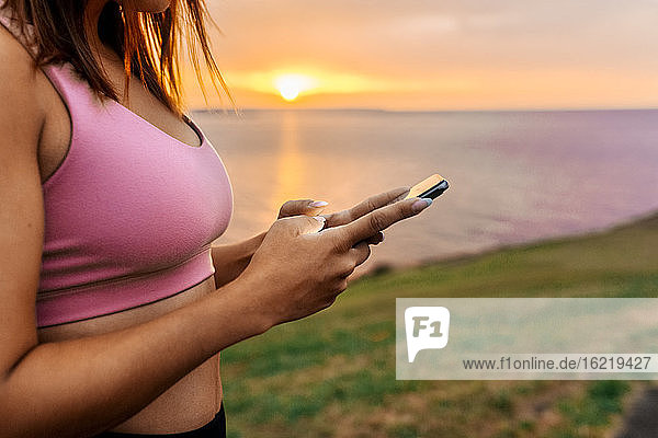 Sportlerin benutzt Smartphone bei Sonnenuntergang