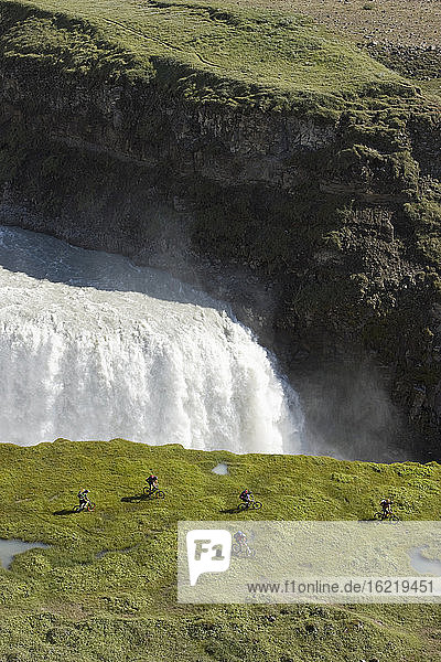 Island  Männer beim Mountainbiking neben einem Wasserfall