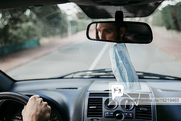 Close-up of protective face mask hanging on rear-view mirror in car