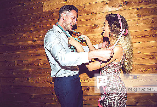 Glücklicher junger Mann und Frau tanzen mit Bändern gegen die Wand in einer Party
