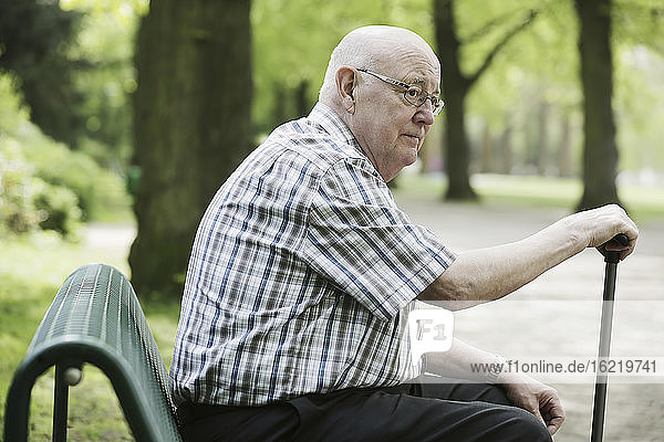 Deutschland  Nordrhein-Westfalen  Köln  Älterer Mann auf Bank sitzend mit Spazierstock im Park