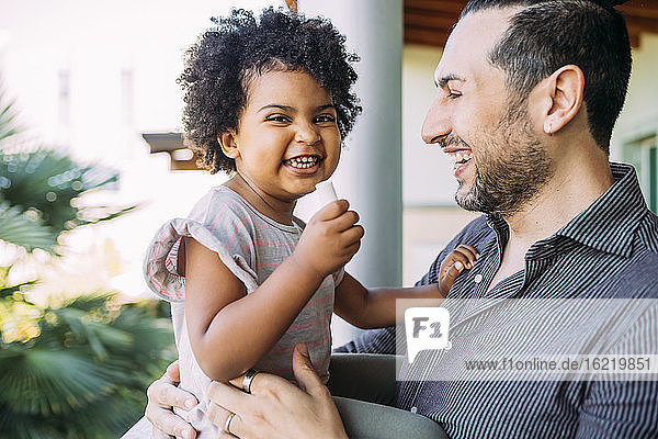 Close-up of man looking at cheerful baby daughter sitting in balcony