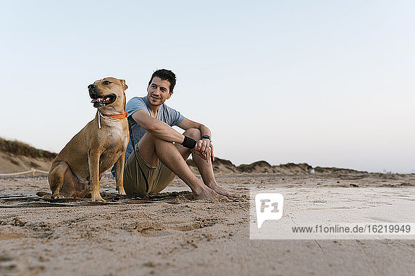 Mann mit seinem Hund am Strand sitzend