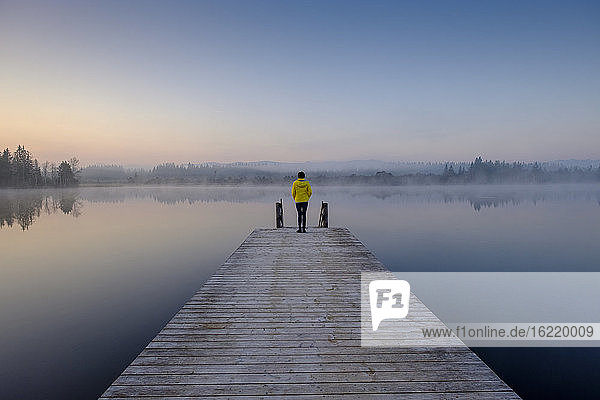 Woman standing at edge of lakeshore jetty at foggy dawn