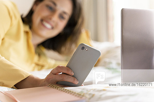 Lächelnde Frau mit Smartphone im Schlafzimmer