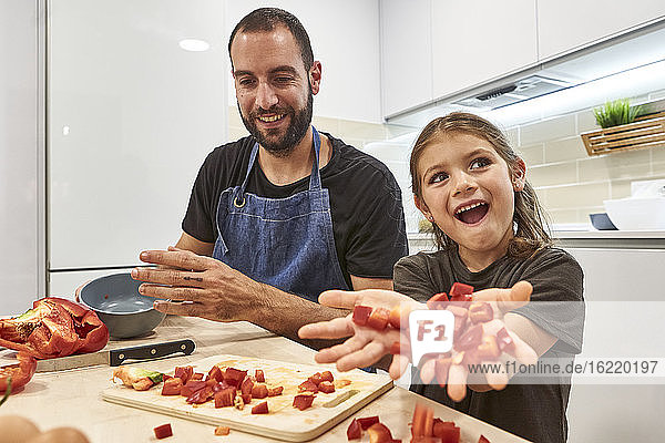 Glücklicher Vater und Tochter mit Paprikastreifen auf dem Tisch bei der Zubereitung von Speisen in der Küche