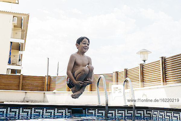 Aufgeregter Junge springt im Pool gegen den Himmel im Sommer