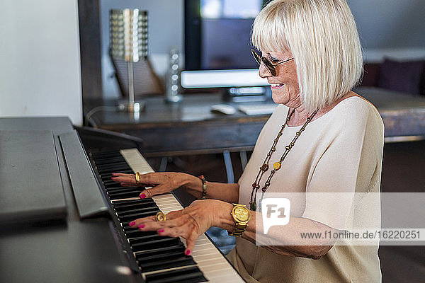 Lächelnde ältere Frau mit Sonnenbrille  die zu Hause sitzend Klavier spielt