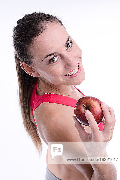 Fröhliche junge kaukasische Frau  die einen roten Apfel isst.