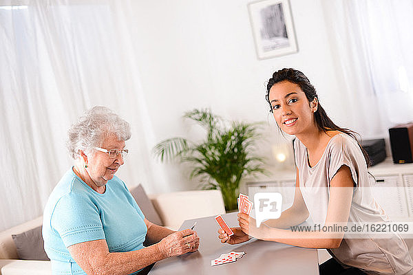 cheerful young girl playing cards with an elderly senior woman