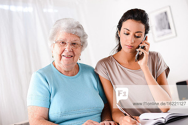 Fröhliche junge Frau  die einer älteren Person beim Papierkram und Telefonieren hilft