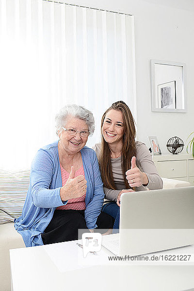 Cheerful young woman helping a senior woman at home with laptop computer