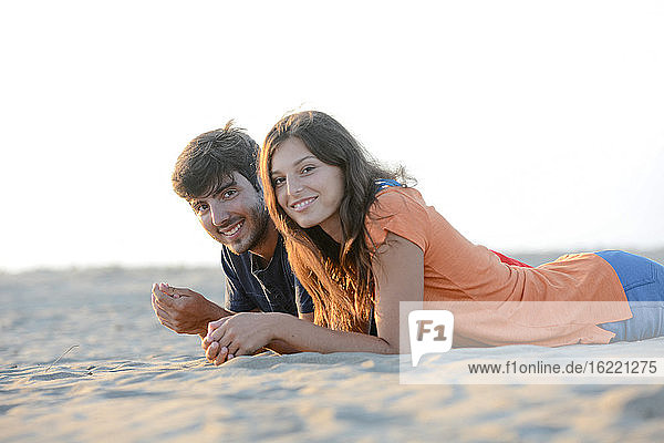 romantisches junges Paar in der Liebe zusammen liegend im Sand am Strand des Mittelmeers Sonnenuntergang