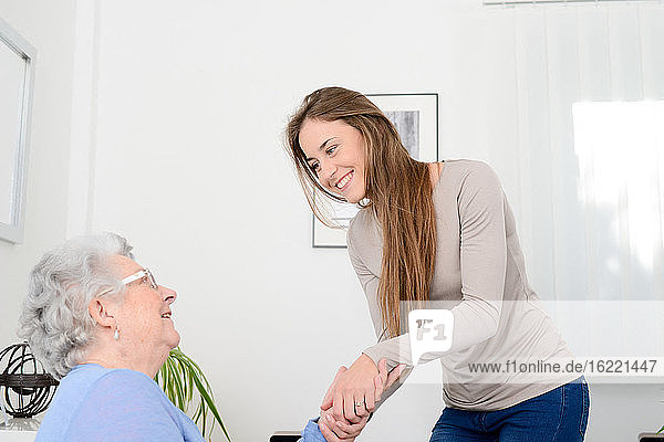 Cheerful young girl taking care of an old senior woman at home