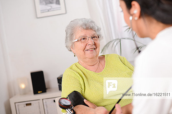 cheerful young female doctor taking blood pressure of an elderly senior woman at home