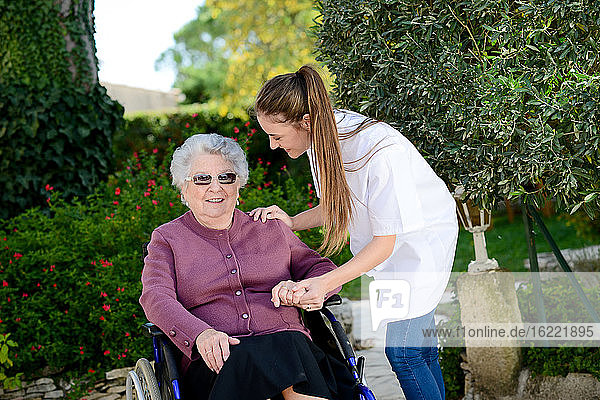 Elderly senior woman on wheelchair with a nurse outdoor in nursing home hospital garden.