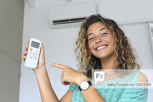 Young woman using a remote control of wall-mounted air conditioner.