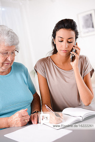 cheerful young woman helping an old senior person doing paperwork and telephone call