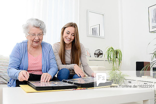 elderly woman with her young granddaughter at home looking at memory in family photo album