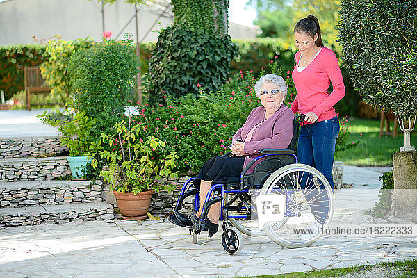 Fröhliche junge Frau im Garten eines Seniorenheims mit einer älteren Dame.