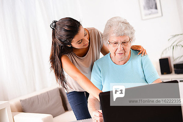 cheerful young woman helping an elderly senior person using laptop computer for internet search and email