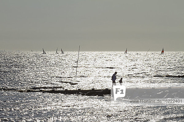 Frankreich  Les Moutiers-en-Retz  44  Mann und Kind gehen hinter einem Spike den Strand hinauf. Beiboote am Horizont.
