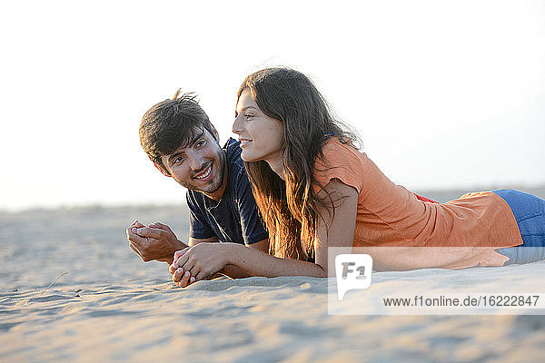 romantisches junges Paar in der Liebe zusammen liegend im Sand entlang des Strandes des Mittelmeers Sonnenuntergang