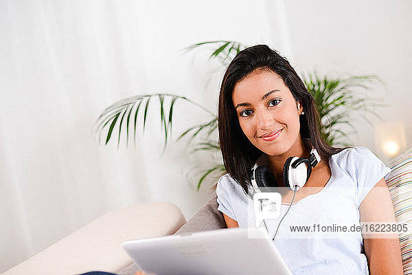 isoliert schöne und fröhliche junge brünette Frau hört Musik mit Tablet-Computer auf Sofa zu Hause