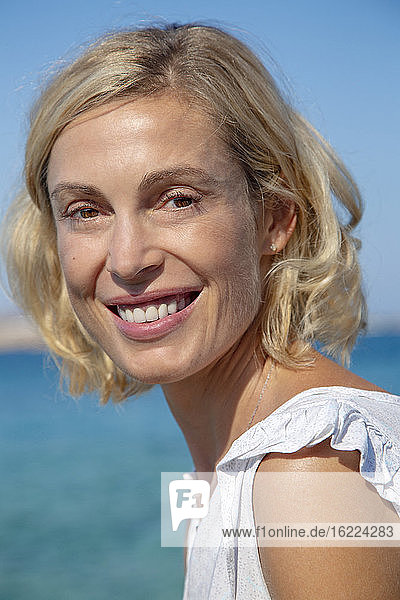 Portrait of a smiling blonde woman in front of the sea.