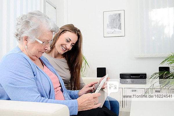 cheerful young girl sharing time with old senior woman and teaching internet with computer tablet
