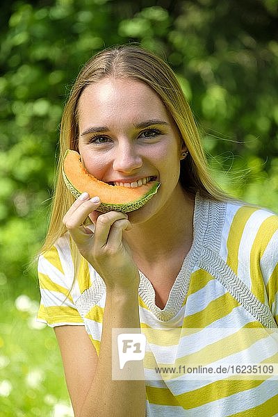 Portrait young blonde woman  biting into a melon  fruit  summer  Bavaria  Germany  Europe