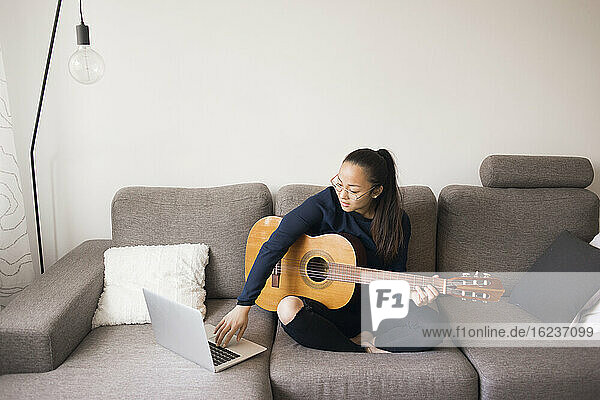 Frau hält Gitarre auf Sofa