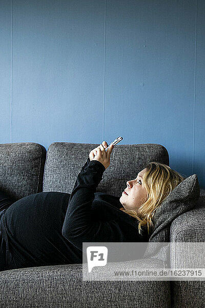 Schwangere Frau telefoniert auf dem Sofa