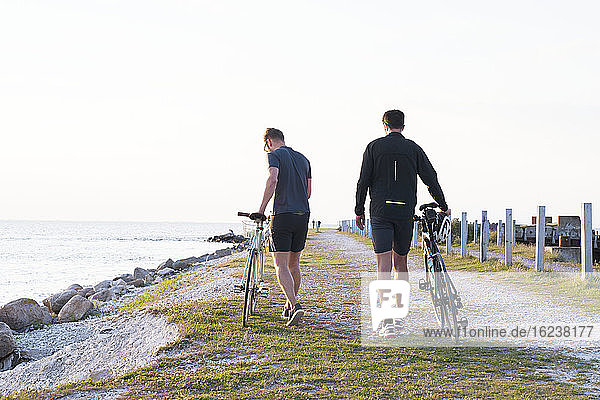 Men walking with bikes at sea
