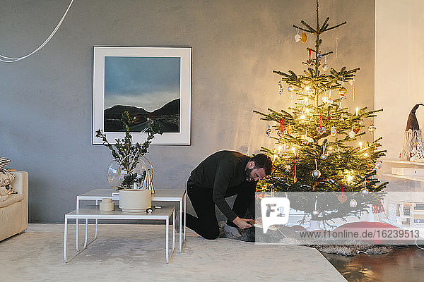 Mann legt Geschenk unter den Weihnachtsbaum