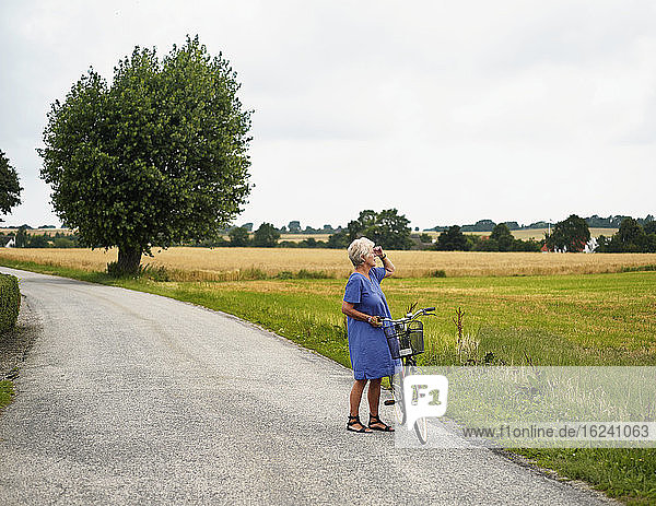 Elderly woman with bicycle by field