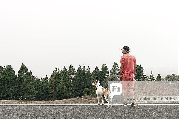 Mann mit Hund am Straßenrand stehend