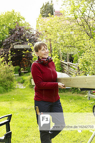 Frau im Garten  die eine Planke trägt