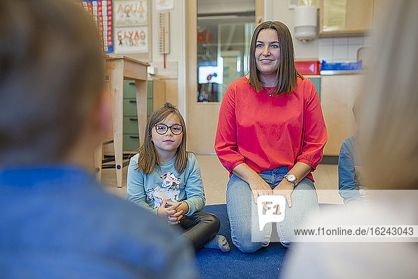 Lehrerin sitzt mit Schülerin auf dem Boden