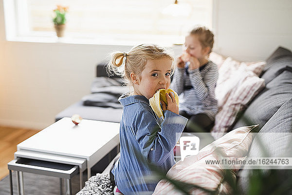 Mädchen isst Banane auf Sofa
