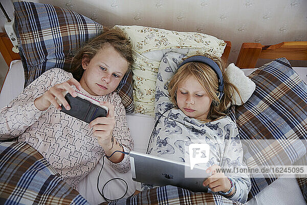 Schwestern im Bett mit digitalen Geräten