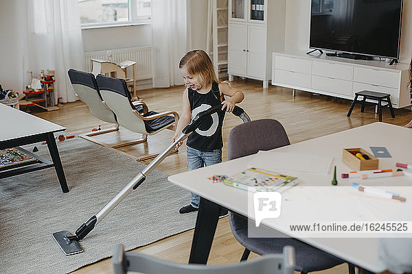 Smiling girl vacuum cleaning living room