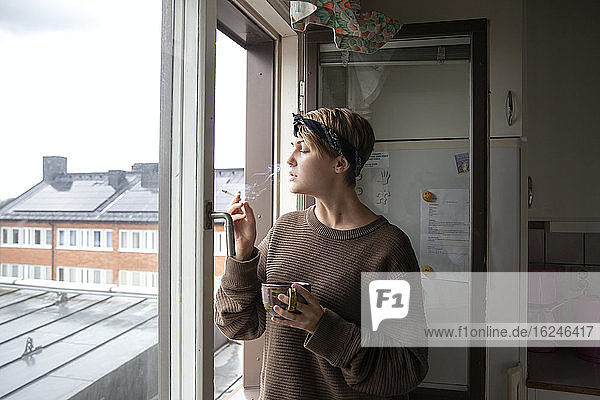 Frau raucht Zigarette am Fenster