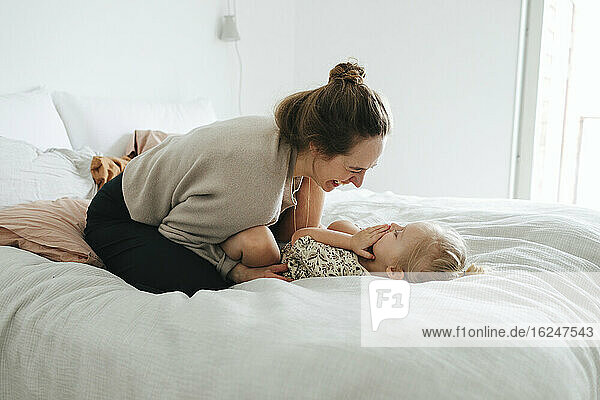 Mother playing with daughter on bed
