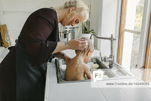 Mother washing baby in kitchen sink