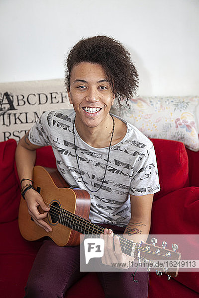 Young man playing guitar on sofa