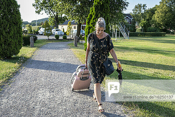 Frau zieht Koffer in der Einfahrt